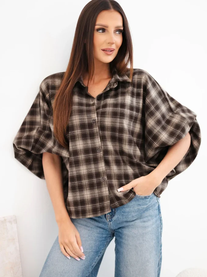 Kobieta nosi brązową koszulę oversize w kratę, jeansy.